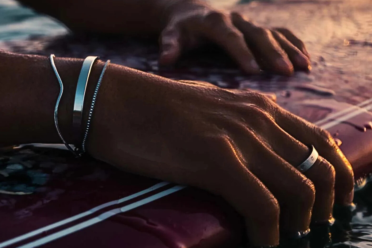 Close-up of a person's hand with bracelets and rings on a textured surface.